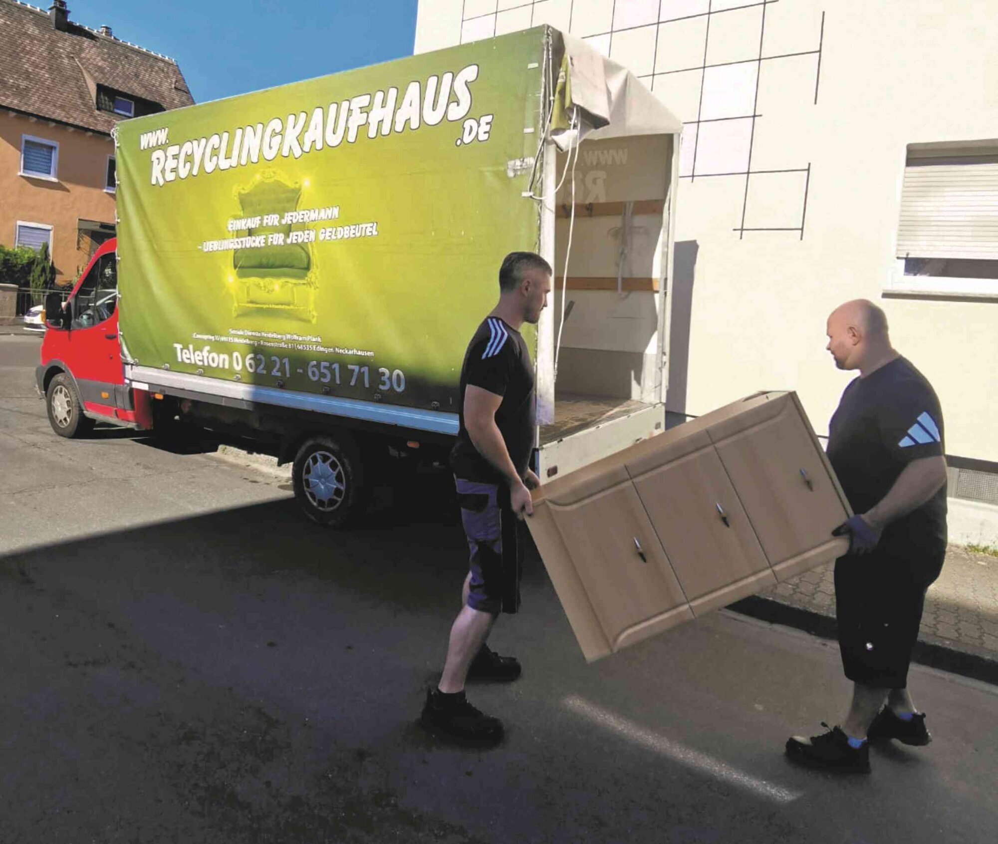 Zwei Mitarbeiter tragen gemeinsam einen Schrank zum Transporter